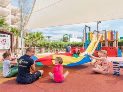 Kinder spielen im Freien mit einem bunten Tuch neben einer Kletter- und Rutschbahn.