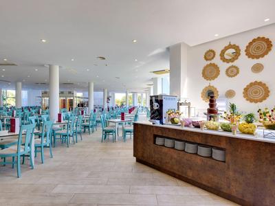 Großer heller Speisesaal mit blauen Stühlen und Buffetbereich mit Dekoration an der Wand.