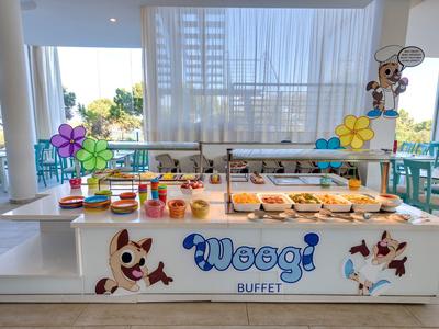 Buffet mit Gebäck, Brot und Sandwiches in hellen, modernen Raum mit cartoonartigen Hundeaufklebern.