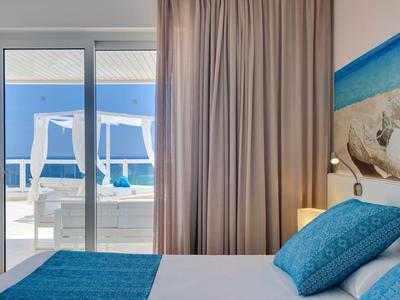 Schlafzimmer mit blauem Bett, Kopfkissen und Zugang zu Balkon mit Meerblick.