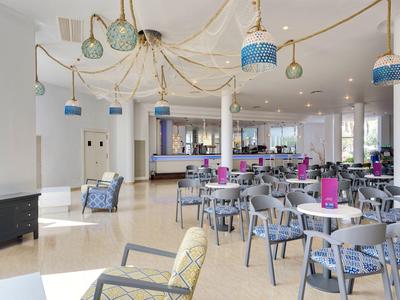 Moderner Gastraum mit vielen runden Tischen, Stühlen in Grau-Blau und dekorativen Lampen an der Decke.