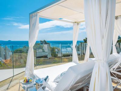 Luxuriöse Terrasse mit weißen Vorhängen und Liegestühlen mit Meerblick.