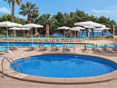 Runder Pool mit blauer Wasserfläche, umgeben von Liegestühlen und Sonnenschirmen neben einem größeren Pool.