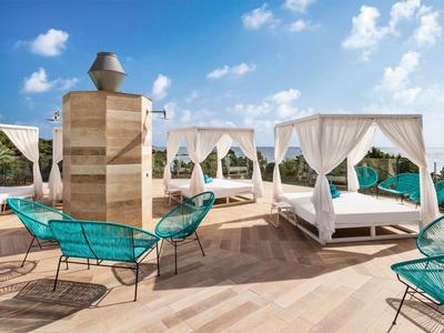 Ein luxuriöser Außenbereich mit Hängesesseln, Himmelbetten und Blick auf das Meer unter blauem Himmel.