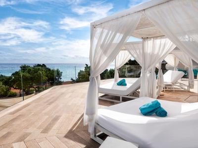 Weiße Daybeds mit türkisfarbenen Handtüchern auf einer Terrasse mit Meerblick.