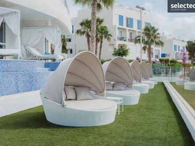 Weiße runde Liegen mit Sonnendächern am Pool in einer modernen Hotelanlage.