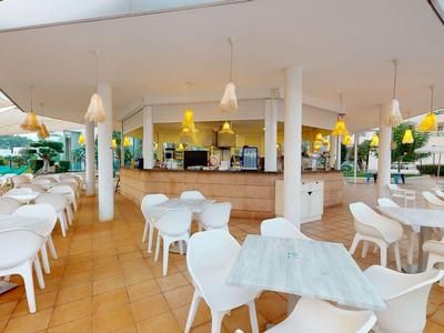 Freiluft-Café mit weißen Tischen und Stühlen sowie einer Bar unter einem großen Pavillon.