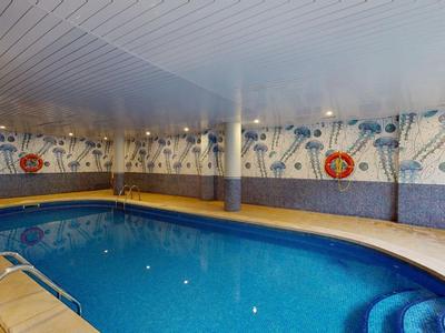 Innenpool mit blauer Wasserfläche und umlaufender Sitzbank in einem Raum mit gemusterten Wänden.