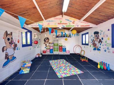 Bunter Kinderspielraum mit Wandmalereien, Matten, Spielzeug und bunten Fahnen unter Holzdach.