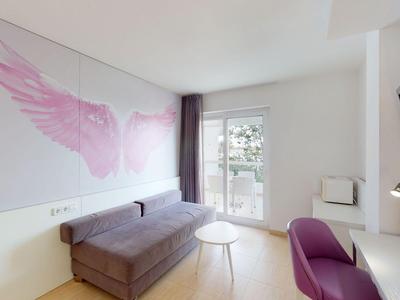 Modernes Hotelzimmer mit rosa Dekoration, Sofa, Schreibtisch und Balkon mit Blick ins Grüne.