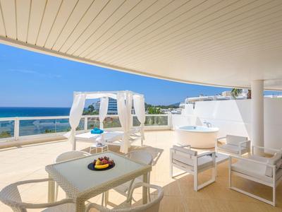 Moderne Terrasse mit Meerblick, weißer Pergola und Essbereich bei Sonnenschein.