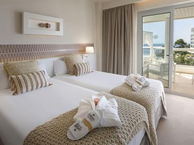 Helles Hotelzimmer mit zwei Einzelbetten, dekorativen Kissen und Zugang zu Balkon mit Aussicht.