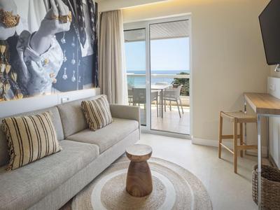 Modernes Hotelzimmer mit Sofa, kleinem Holztisch und Balkon mit Meerblick.