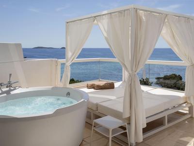 Terrasse mit Whirlpool und Himmelbett mit Meerblick bei klarem Himmel.
