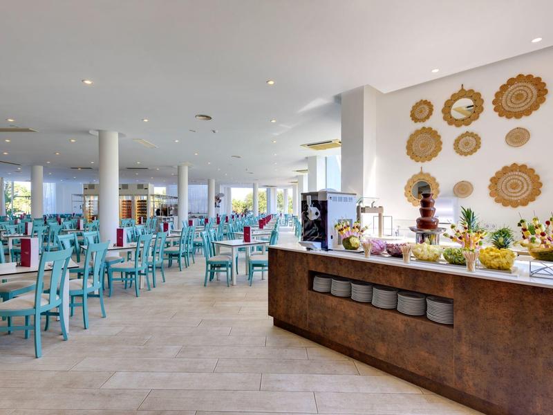 Großer heller Speisesaal mit blauen Stühlen und Buffetbereich mit Dekoration an der Wand.