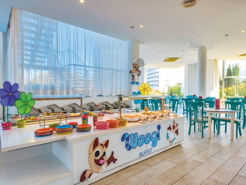 Bunt dekoriertes Buffet mit Kuchen in hellem, modernem Raum und großen Fenstern, blauer Stühle.