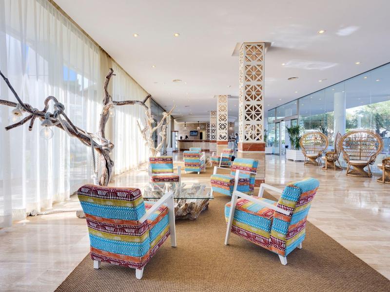 Heller moderner Raum mit bunten Sesseln, großen Fenstern, hängenden Rattanstühlen und Holzdekor.