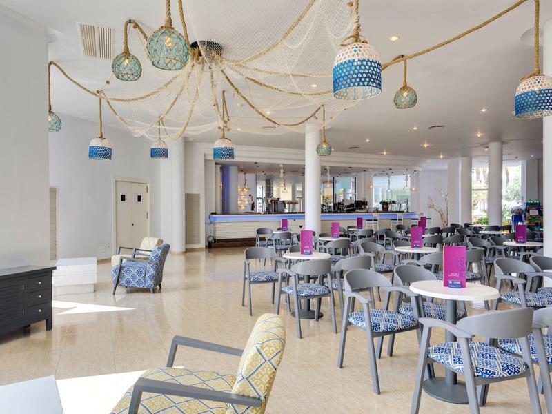 Moderner Gastraum mit vielen runden Tischen, Stühlen in Grau-Blau und dekorativen Lampen an der Decke.