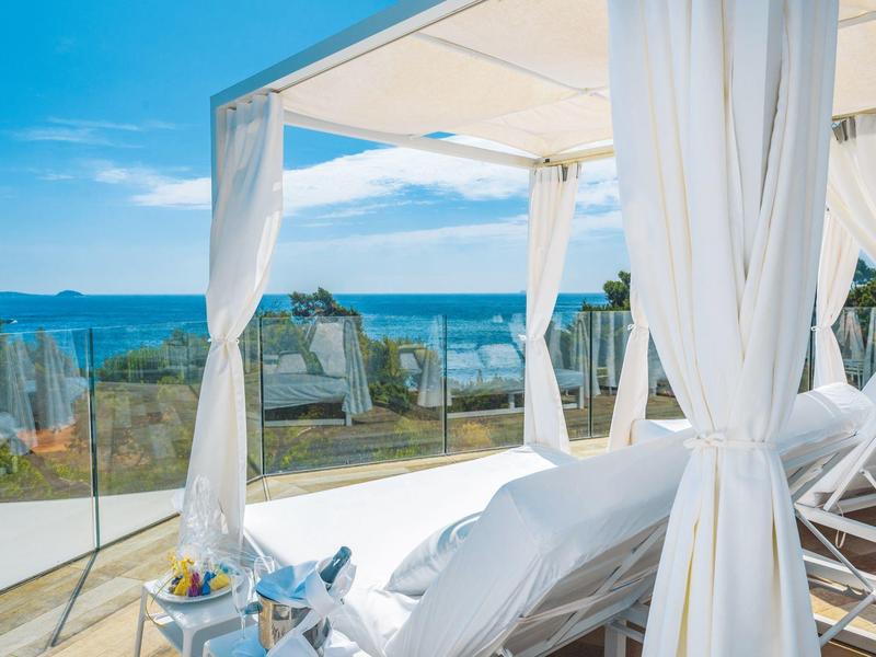 Luxuriöse Terrassen mit weißen Liegen, Glasgeländer, Meerblick und klarem blauem Himmel.