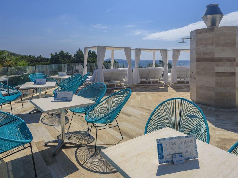 Dachterrasse mit blauen Stühlen, Tischen und weißen Sonnensegeln bei klarem Himmel.