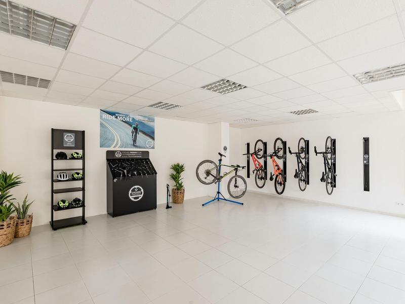 Helle, moderne Fahrradwerkstatt mit weißen Wänden, Werkzeugwand, Fahrradständer und Pflanzen in Töpfen.