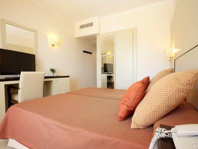 Moderner Hotelraum mit Doppelbett, brauner Bettwäsche, Flachbildschirm und hellem Interieur.