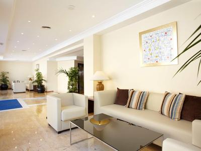 Heller Wohnzimmerbereich mit beige Wänden, grauen Sofas, Dekokissen und grünen Zimmerpflanzen.