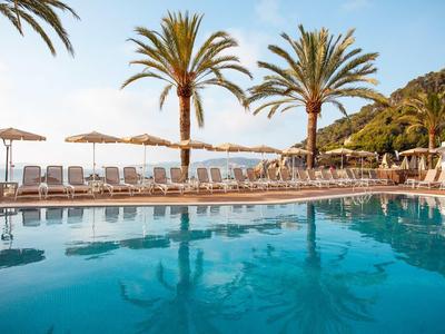 Blauer Pool mit Liegestühlen, Sonnenschirmen und Palmen unter klarem Himmel am Meer.