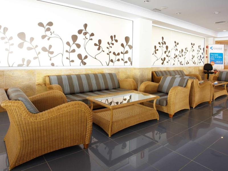 Hell eingerichteter Sitzbereich mit Flechtmöbeln und floraler Wanddekoration in hellem Raum.