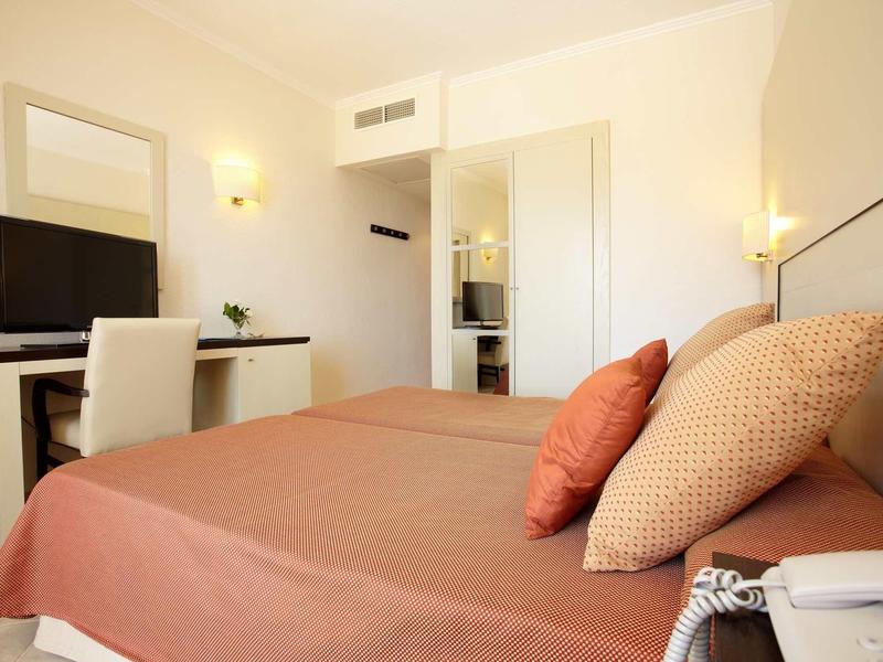 Moderner Hotelraum mit Doppelbett, brauner Bettwäsche, Flachbildschirm und hellem Interieur.