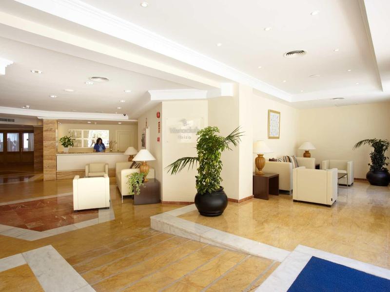 Heller Hotellobby mit weißen Sesseln, großen Pflanzen und heller Holz- und Fliesenboden.