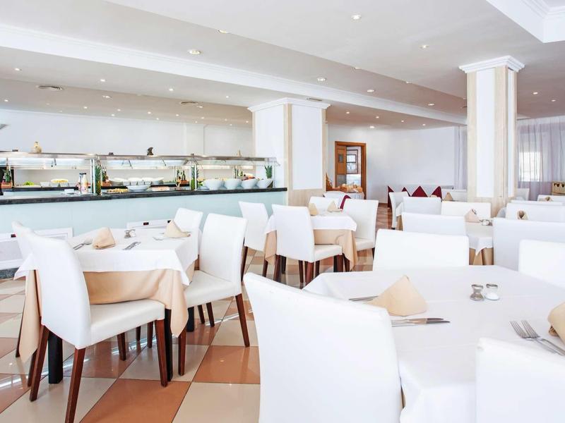 Hell eingerichteter Speisesaal mit weißen Stühlen, Tischen und Buffetbereich im Hintergrund.