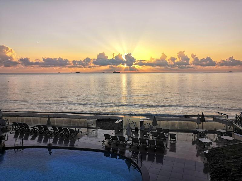 Zachód słońca nad spokojnym morzem z basenem i leżakami na pierwszym planie.