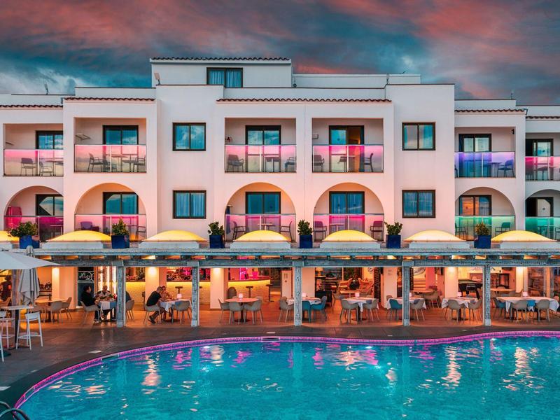 Nowoczesny kompleks hotelowy z podświetlanym basenem i miejscami do siedzenia o zachodzie słońca.