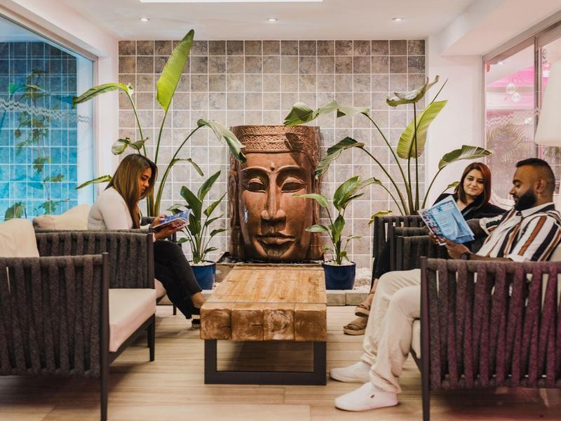 Przytulny salon hotelowy z drewnianym stołem, sofami i uspokajającą głową Buddy na ścianie.