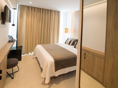 Helles Hotelzimmer mit Doppelbett, braunen Vorhängen, Holzschrank und modernem TV an der Wand.