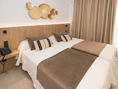 Hell eingerichtetes Doppelzimmer mit zwei Einzelbetten, braunen Decken und stilvoller Wanddekoration.