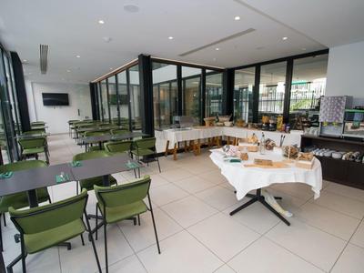 Moderner Speiseraum mit grünen Stühlen, Taschenbuffet auf weiß gedecktem Tisch, große Fenster.