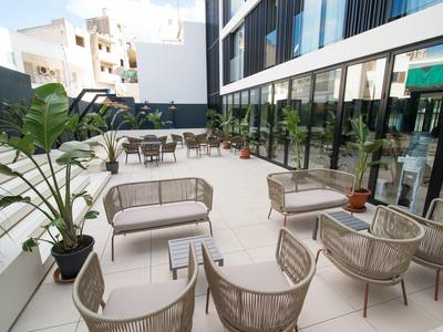 Moderner Außenbereich mit grauen Sesseln, Pflanzen und Glasfenstern an hellem Boden.