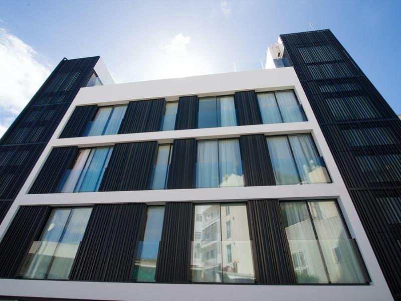 Modernes Gebäude mit großen Glasfenstern und dunklen vertikalen Lamellen unter blauem Himmel.
