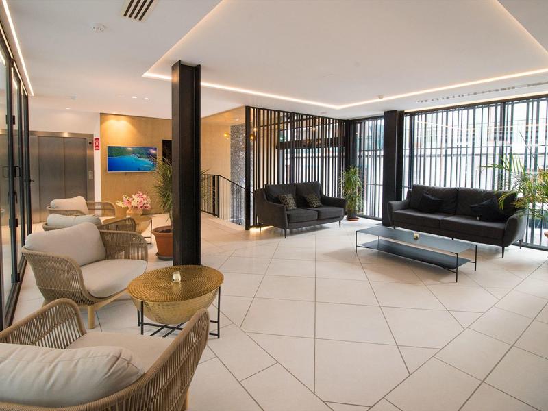 Heller, moderner Wartebereich mit weißen Kacheln, schwarzen Sofas, Stühlen, Tischen und großen Fenstern.