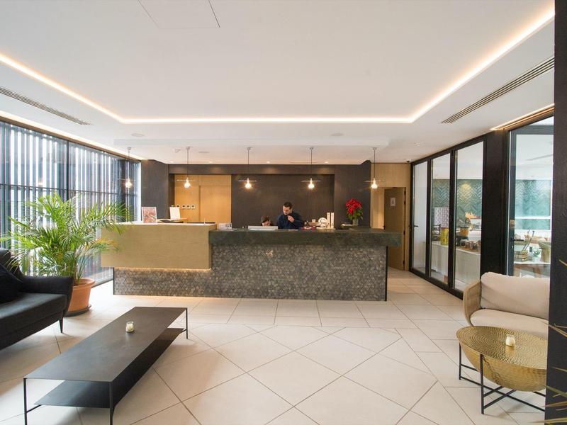 Moderne Hotellobby mit Marmorempfang, Ledersofa, Sessel, Kaffeetisch und großen Fenstern.