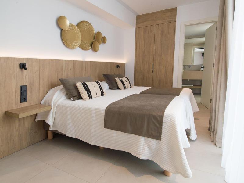 Modernes Schlafzimmer mit großem Bett, hölzernem Kopfteil, kreisförmiger Wanddekoration und hellem Boden.