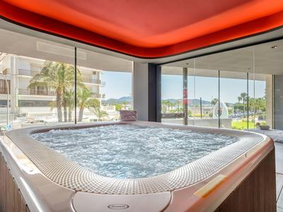 Nowoczesne jacuzzi z bulgoczącą wodą w pomieszczeniu z oknami od podłogi do sufitu i czerwonym oświetleniem sufitowym.