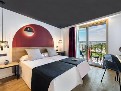 Nowoczesny pokój hotelowy z podwójnym łóżkiem, częścią wypoczynkową i balkonem z widokiem na morze.