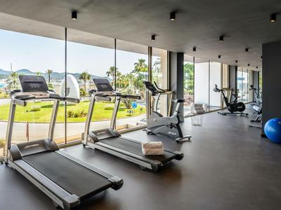 Nowoczesna siłownia z bieżniami i sprzętem fitness przed dużymi oknami z widokiem na zewnątrz.