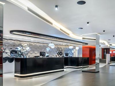 Nowoczesna recepcja hotelowa z czarnym lada i zakrzywionymi białymi światłami sufitowymi.