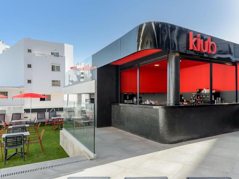 Nowoczesna przestrzeń barowa na zewnątrz z czerwonymi akcentami i miejscami do siedzenia na tarasie.