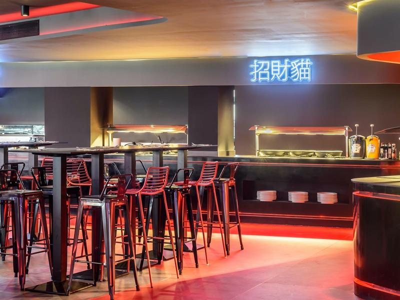 Nowoczesny bar hotelowy z wysokimi stołkami, ladami i atmosferycznym czerwonym i żółtym oświetleniem.