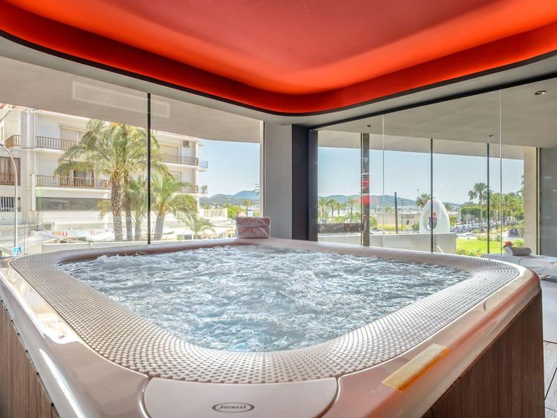 Nowoczesne jacuzzi z bulgoczącą wodą w pomieszczeniu z oknami od podłogi do sufitu i czerwonym oświetleniem sufitowym.